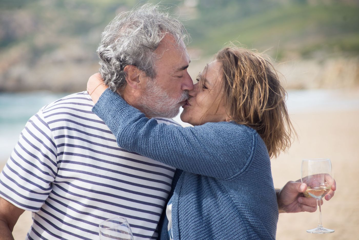 Mature couple sharing a kiss on the beach with wine glasses