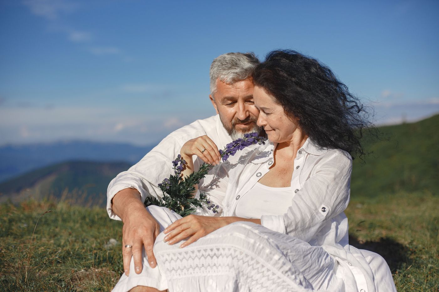 Mature couple sitting on a grassy hillside with wildflowers